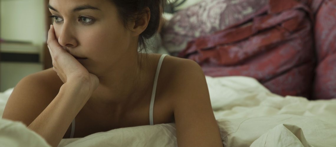 Young woman looking away in thought on bed with hand under chin, portrait